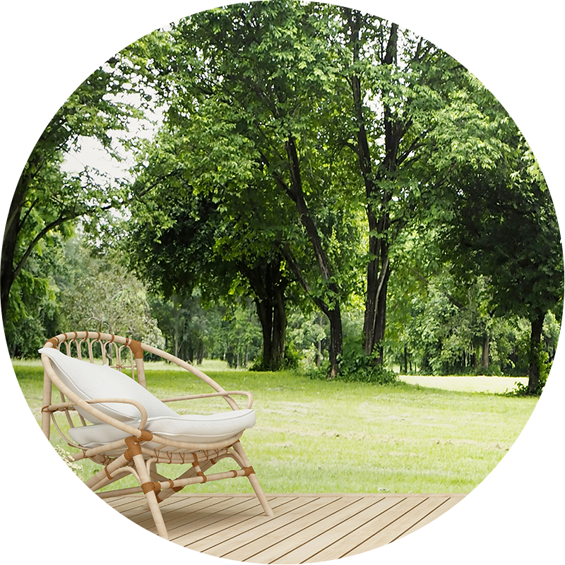 Round chair sitting on a deck with large trees in a yard. 