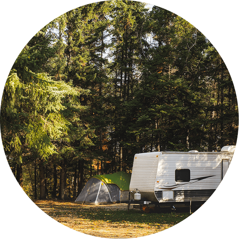 Wooded camping area with a tent and RV setup in an open space. 