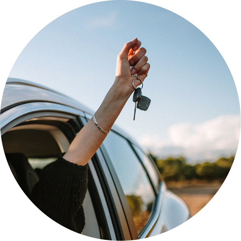 Woman holding car keys outside of her car window in an excited way. The image is inside of a circle shape.