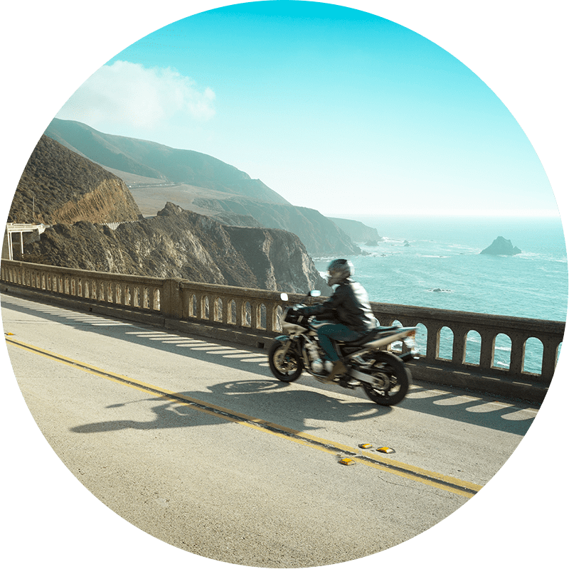 Motorcycle driving on a cliffside road near the ocean. 