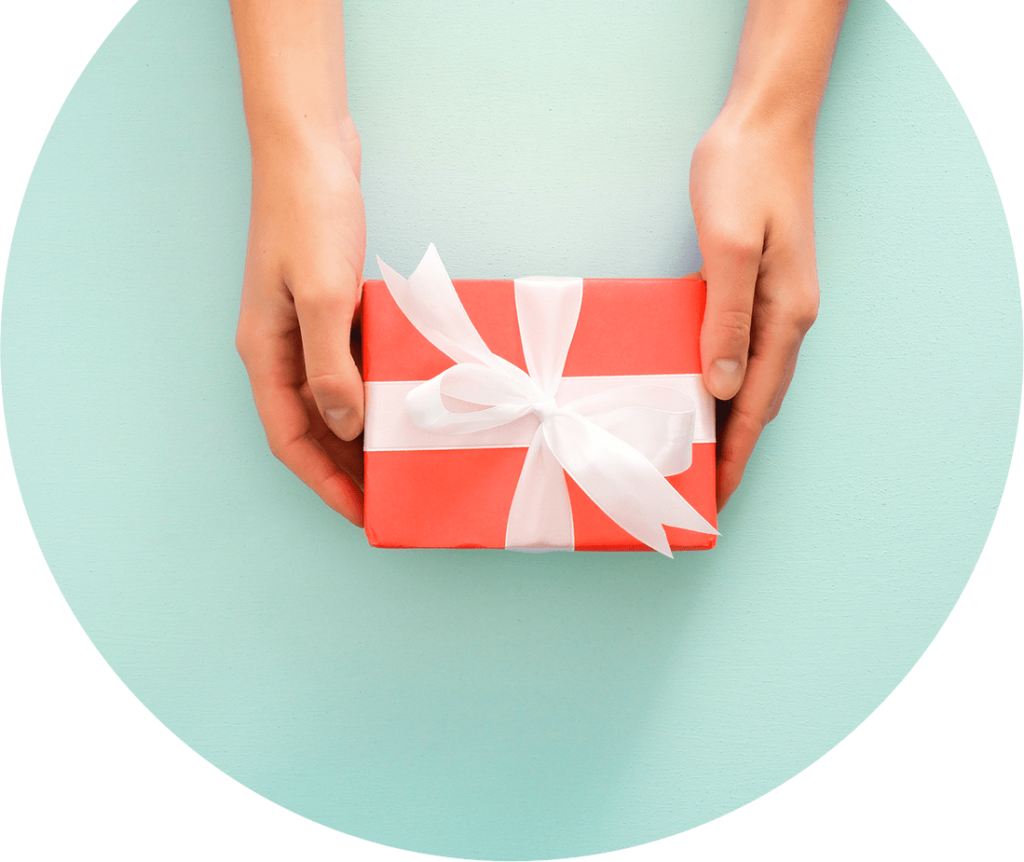 Someone holding out an orange-colored gift wrapped in a white bow. Image is inside of a circle shape.