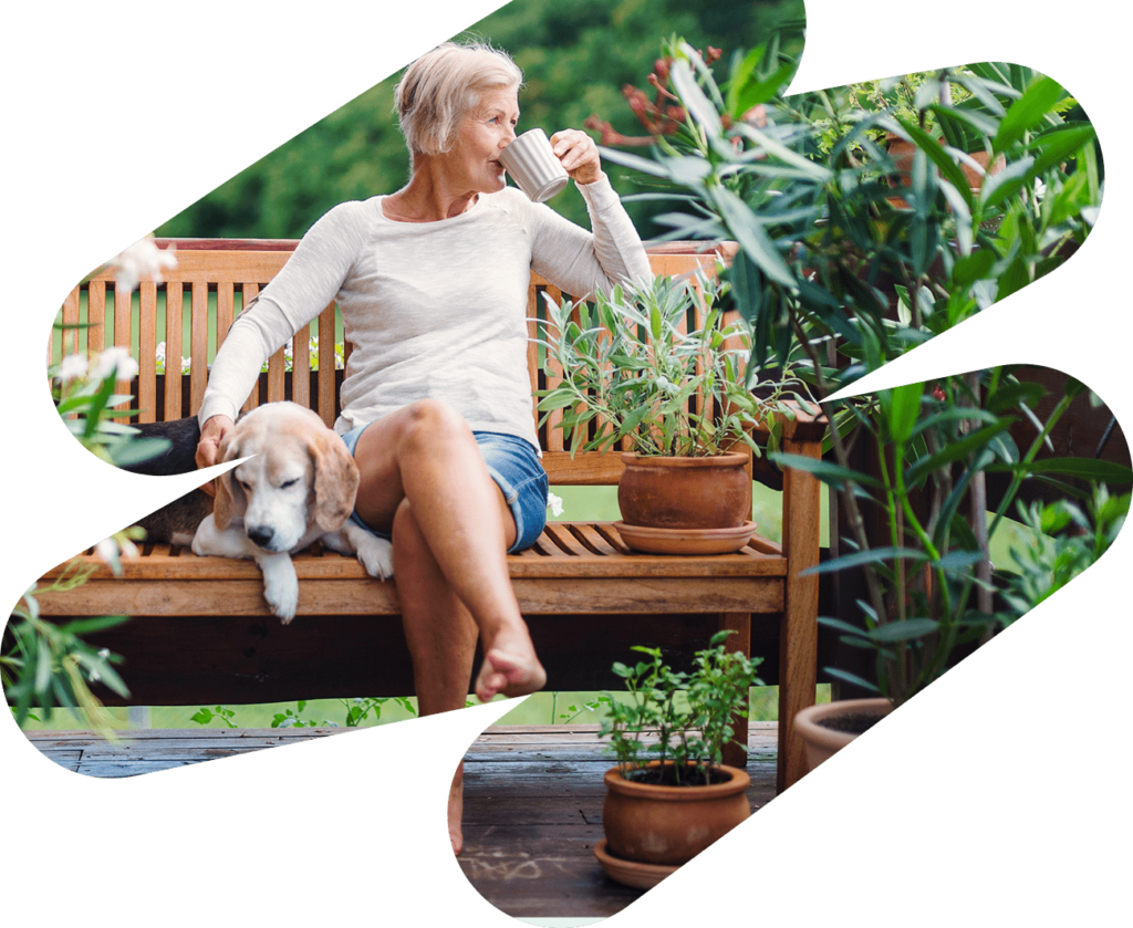 Woman enjoying a cup of coffee while sitting on her deck with her dog. Image is inside of a swish shape.