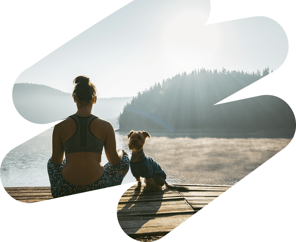 Woman wearing exercise clothing sitting with her dog on the dock of a lake looking into the distance