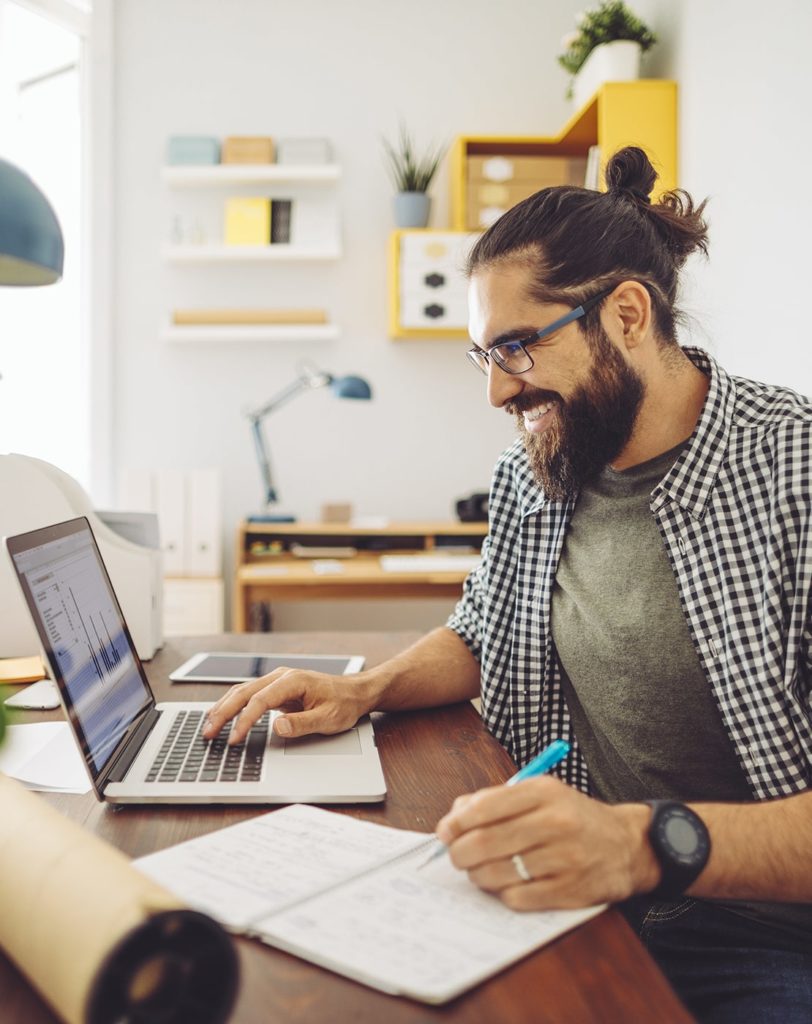 Man with hair in bun smiling while working on his computer in his modern office.