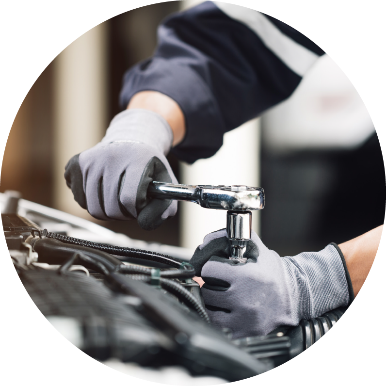 A mechanic repairing a car with gloves on holding a wrench against car. Photo is inside of a circle shape.