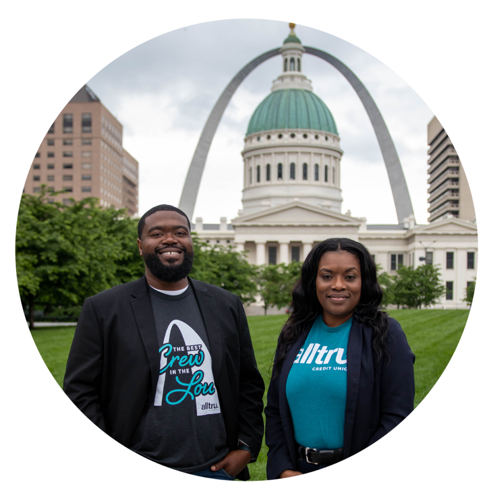 Alltru Financial Empowerment Coordinators Kenneth and Stephanie, pictured smiling in front of the St. Louis Arch with Alltru shirts. Photo is inside of a circle shape.