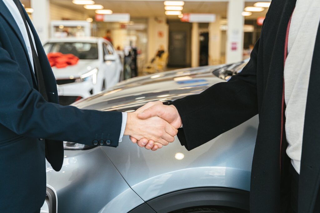 A man shaking hands with his car salesman with his new gray car in the background