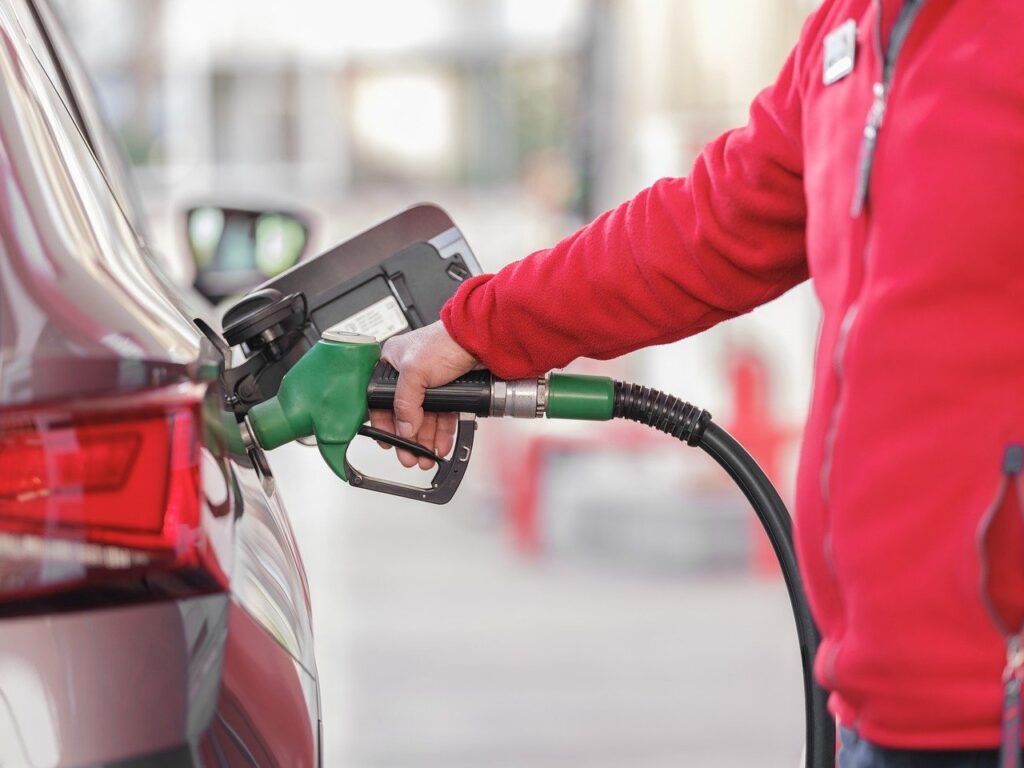 A man in a red zip-up jacketing pumping gas in his car