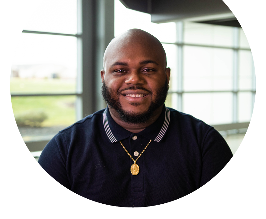 Rewards Checking | Alltru Credit Union | St. Louis, MO Alltru member Sean in a black polo with a gold necklace, smiling inside an Alltru branch