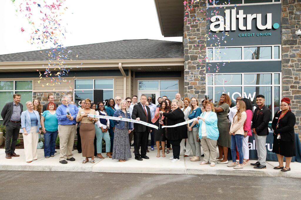A group of Alltru employees, leaders, and community members cutting the ribbon outside the Florissant branch with confetti in the air