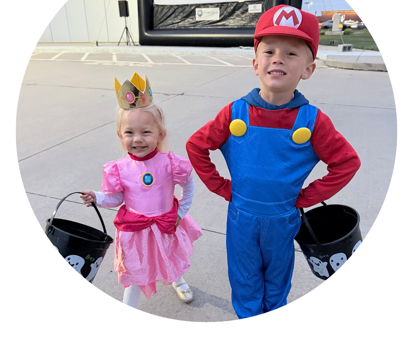 A cut circle photo of young members Ava and Jackson in Halloween costumes as Princess Peach and Super Mario